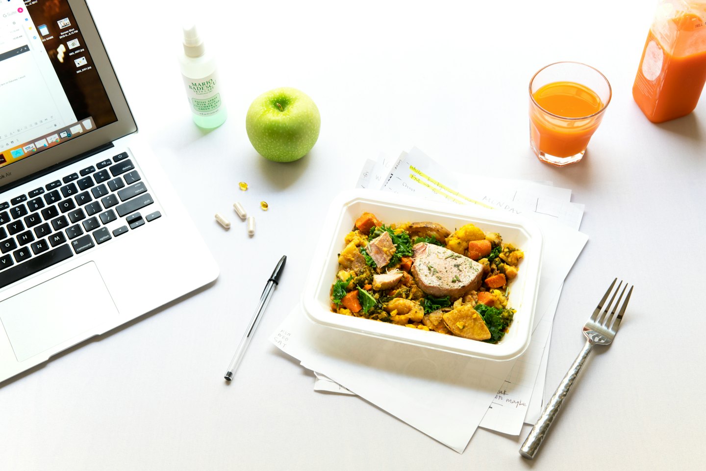 Zdrowy lunch i materiały biurowe na białym biurku.