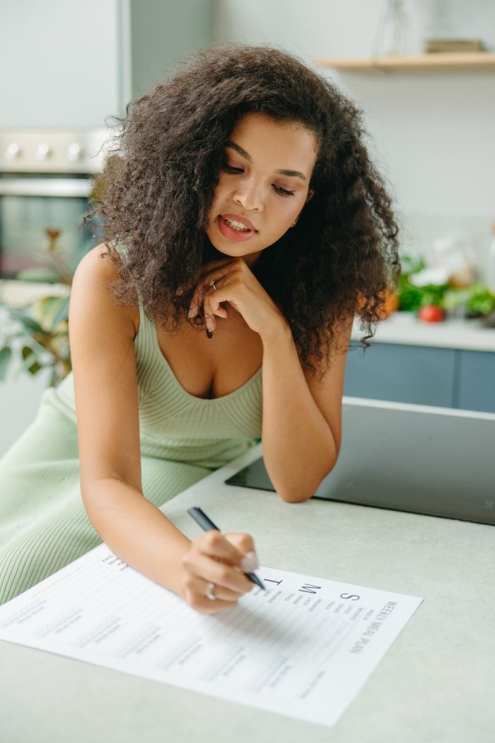 Young woman with curly hair planning a healthy meal indoors. Focus on meal planning and lifestyle.